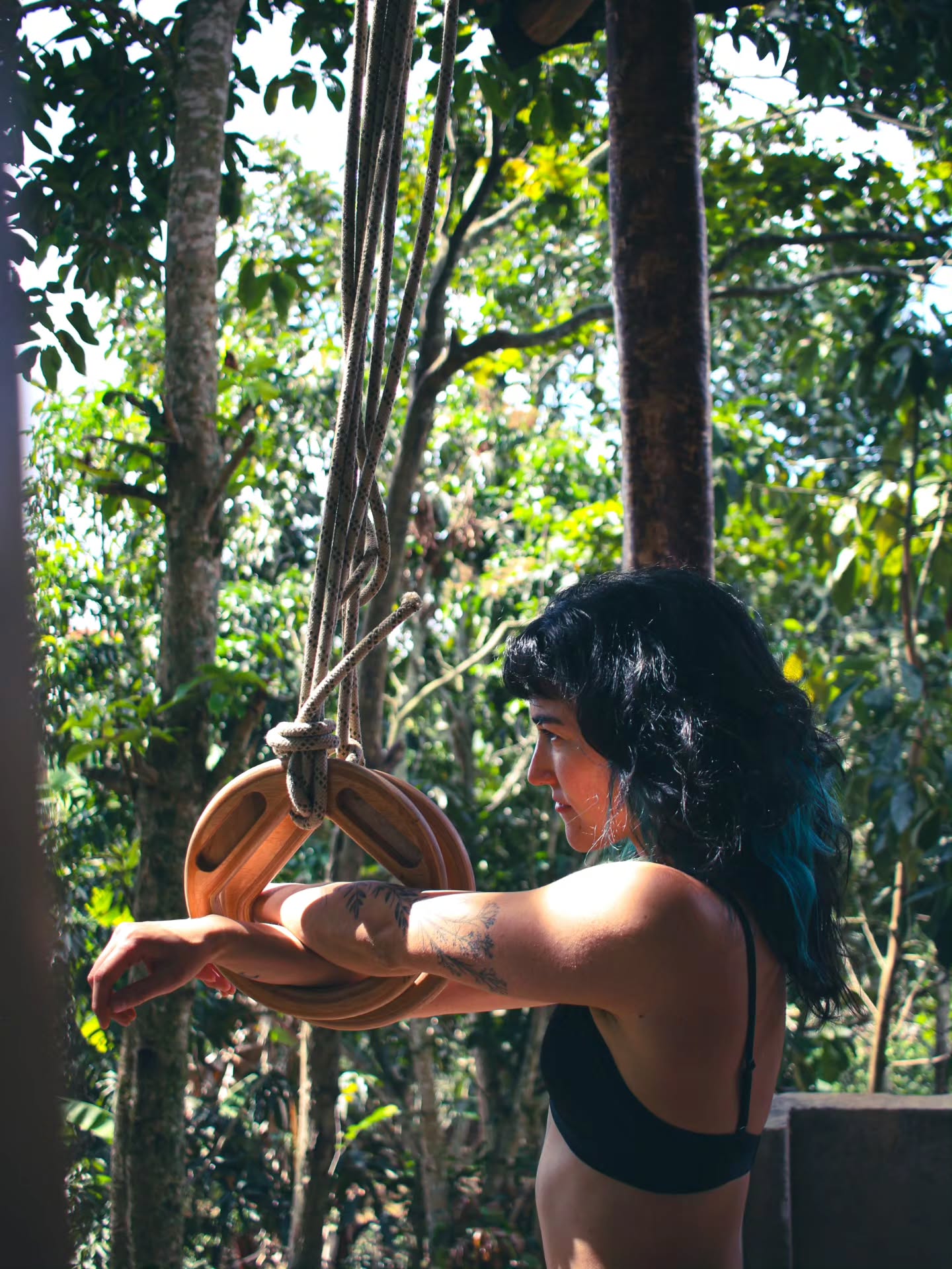 Pilar Waters in profile, holding gymnastic rings hung in a jungle, arms extended forward in a controlled pose.